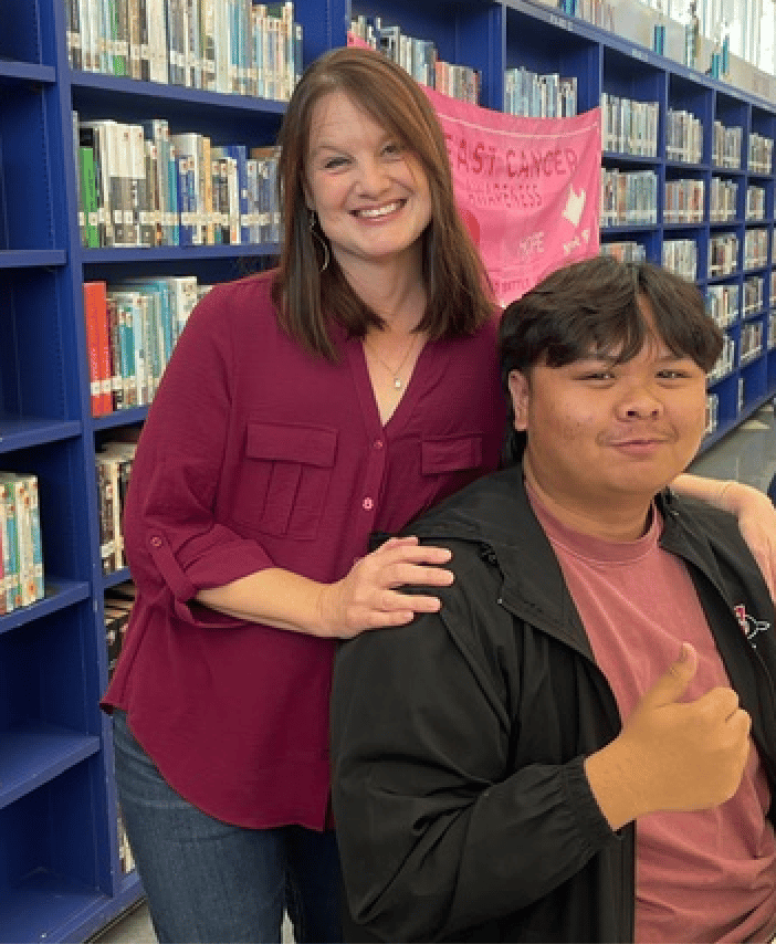 Jenny with a student at a school library event, breast cancer awareness banner behind them